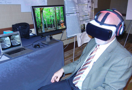 man wearing goggles with scenes of nature on computer screens behind him